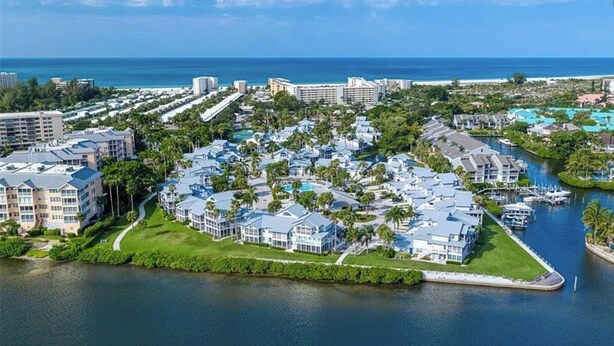 Un complejo turístico frente al mar con varias construcciones, un puerto deportivo y una extensión de agua.