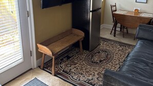 Ett kompakt vardagsrum med en platt-TV som hänger på väggen, ett svart kylskåp, en träbänk, ett matbord med stolar och en mönstrad matta.
