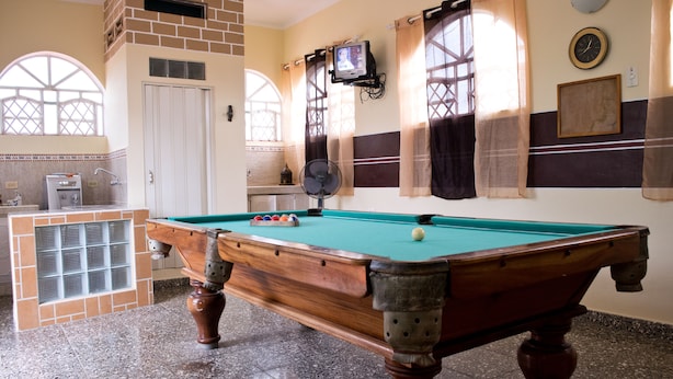 A pool table in a room with a tiled floor, a small bar area, and a window with curtains. - Hostal Bola 8 (Remedios)