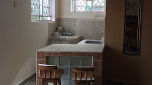 A compact kitchen with a sink, two stools, and a window with a lattice design. - Hostal Bola 8 (Remedios)