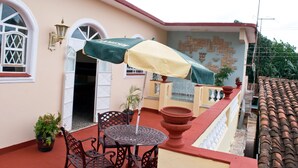 A patio with a table and chairs, a covered umbrella, and a wall with a mosaic design. - Hostal Bola 8 (Remedios)