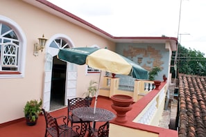 A patio with a table and chairs, a covered umbrella, and a wall with a mosaic design. - Hostal Bola 8 (Remedios)