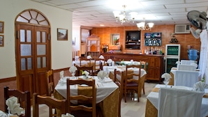 A restaurant with wooden tables and chairs, a bar area, and a television. - Hostal Bola 8 (Remedios)