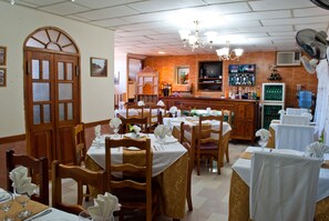 A restaurant with wooden tables and chairs, a bar area, and a television. - Hostal Bola 8 (Remedios)