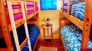 A small, cozy room with bunk beds, a desk with a lamp, and a window with blinds.