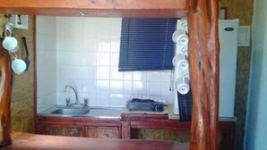 Eine kleine Küche mit Spüle, einem Fenster mit Jalousien und einem Kühlschrank.