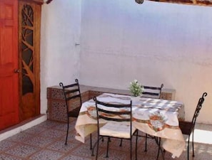 An outdoor patio with a table and chairs, a wooden door with a glass panel, and a tiled floor.