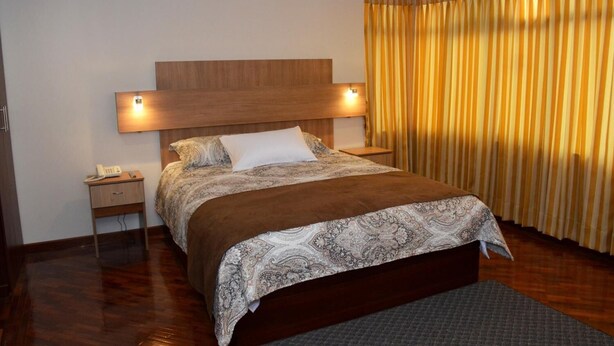 A bedroom with a large bed, a nightstand, a bedside lamp, and a curtain. - Los Angeles Stay Inn (Quito)