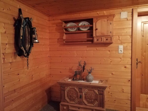 A wooden interior with a wall-mounted clock, a shelf with plates, a cabinet, and a decorative wooden chest.