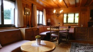 A cozy cabin interior with a round wooden table, cushioned seating, and a chandelier. - Vacation cottage Greber, Austria (Mellau)