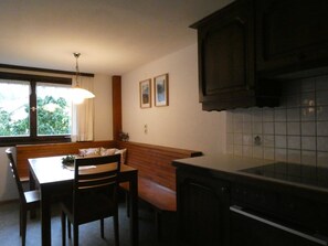 A kitchen with a dining table, chairs, a bench, a hanging light fixture, and a window with curtains.