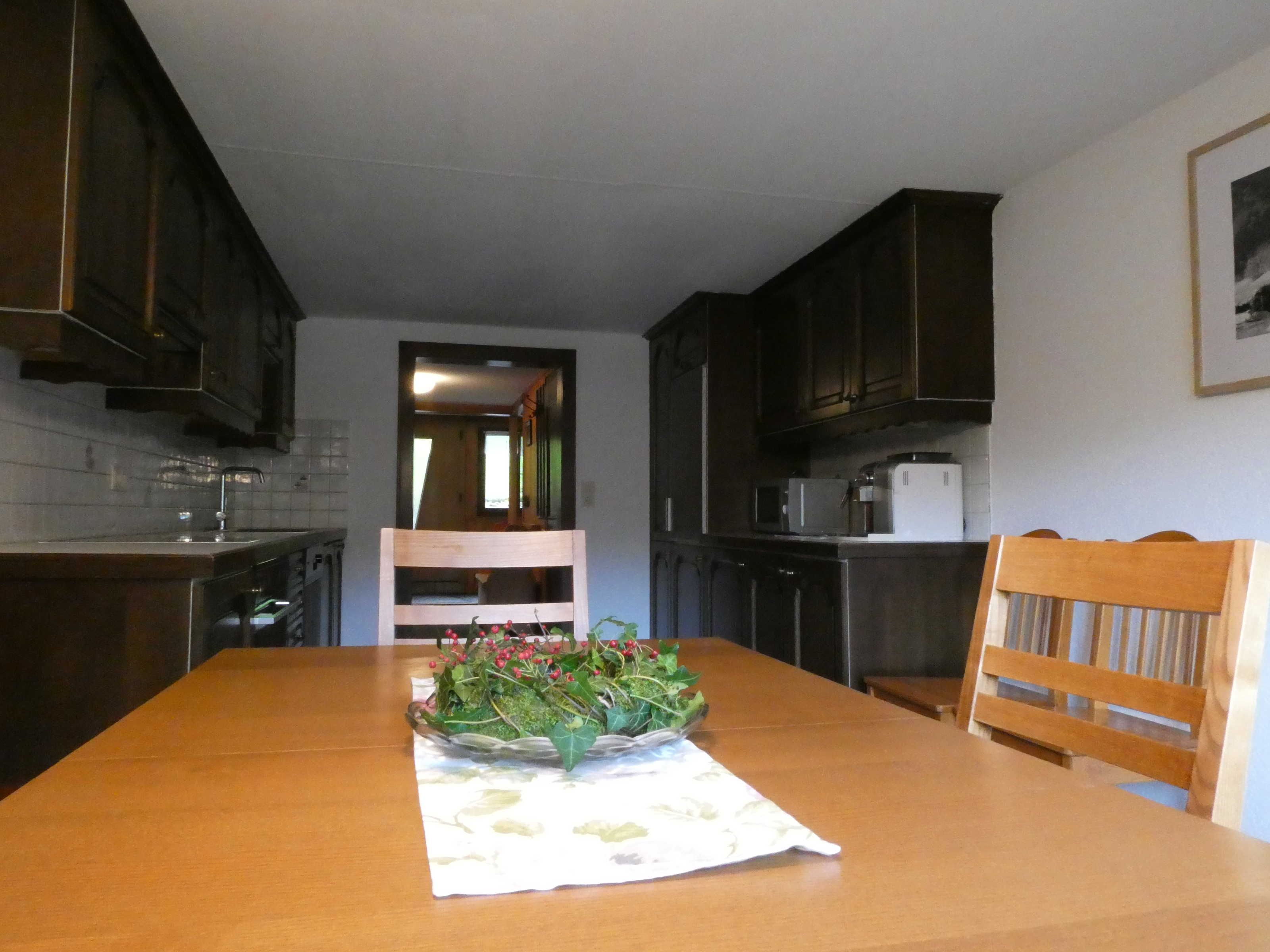Une cuisine avec des meubles de rangement en bois, une table à manger avec un set de table à motifs floraux et une chaise.