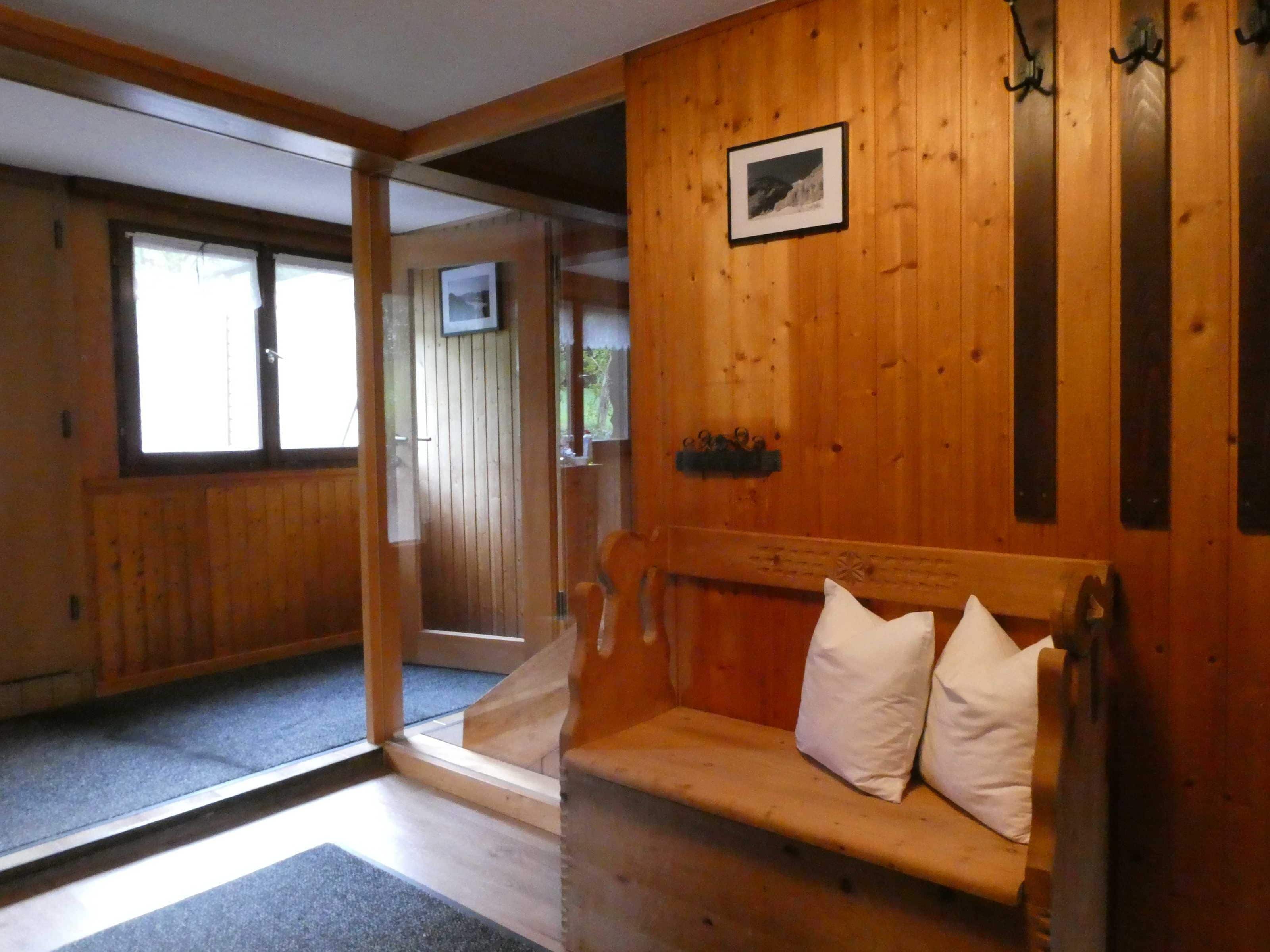Un interior de madera con un banco, un cuadro en la pared y una puerta que da a otra habitación.