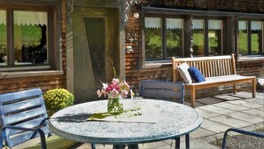 A patio with a round table, chairs, a bench, and a door with a decorative ironwork. - Vacation cottage Greber, Austria (Mellau)