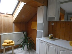 A room with wooden walls, a skylight, a radiator, a plant, and a white cabinet with a towel on a stool.