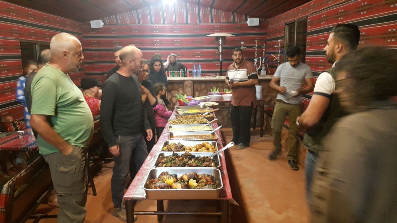 A buffet setup with multiple food trays in a room with striped walls and a tiled floor.