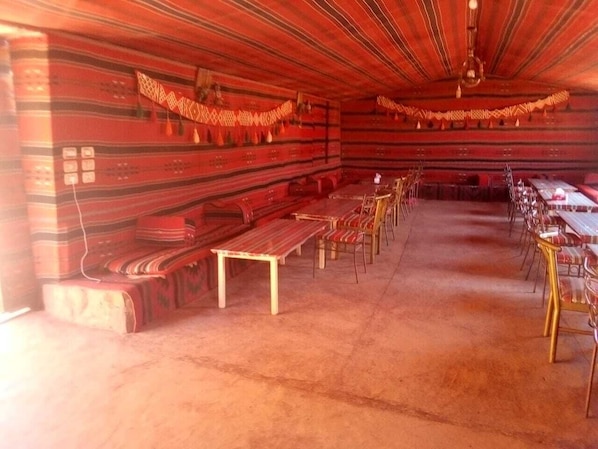 Une pièce aux murs rayés, avec un banc et des tables accompagnées de chaises.