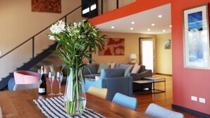A dining area with a wooden table, a vase with flowers, and a bottle of wine. - Cove View Retreat St.Helens (St Helens)
