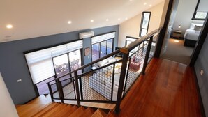 A modern interior with a wooden staircase, a balcony with outdoor furniture, and a bedroom with a bed and nightstand. - Cove View Retreat St.Helens (St Helens)