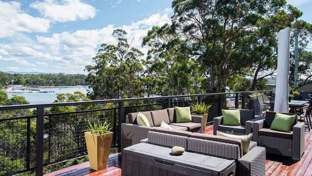 A deck with outdoor furniture, a view of a lake, and trees in the background. - Cove View Retreat St.Helens (St Helens)