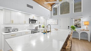 Una cocina moderna con armarios blancos, una isla grande y techo de madera.