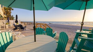 Un patio frente a la playa con sillas Adirondack verdes y una mesa, con vista al océano.
