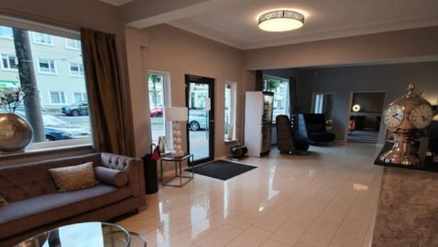 A hotel lobby with a sofa, a coffee table, a clock, and a view of the street outside. - artHotel Bremen (Bremen)
