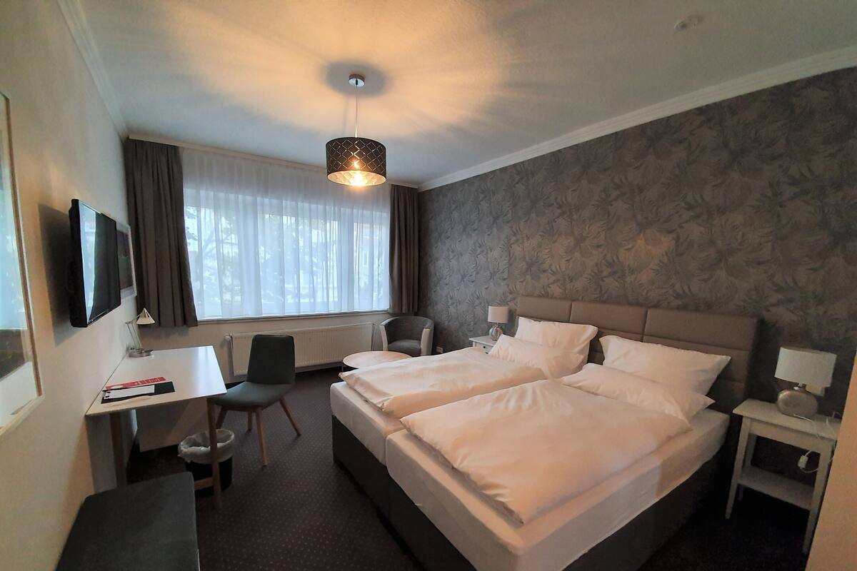 A hotel room with a bed, desk, chair, and a television.