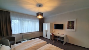 A hotel room with a bed, a desk, a chair, a TV, and a window with curtains. - artHotel Bremen (Bremen)