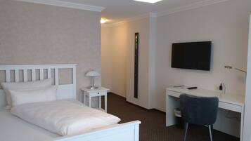 Quarto de hotel com cama, escrivaninha, cadeira, televisão e abajur.