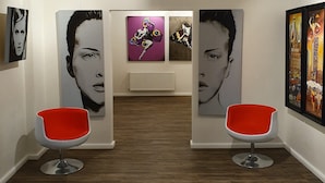 A hallway with two red chairs, white walls, and framed artworks on the walls. - artHotel Bremen (Bremen)