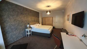A hotel room with a bed, a desk, a chair, a TV, and a wardrobe.