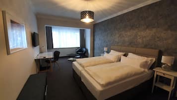 Habitación de hotel con dos camas, un escritorio, una silla, un televisor y una ventana con cortinas.