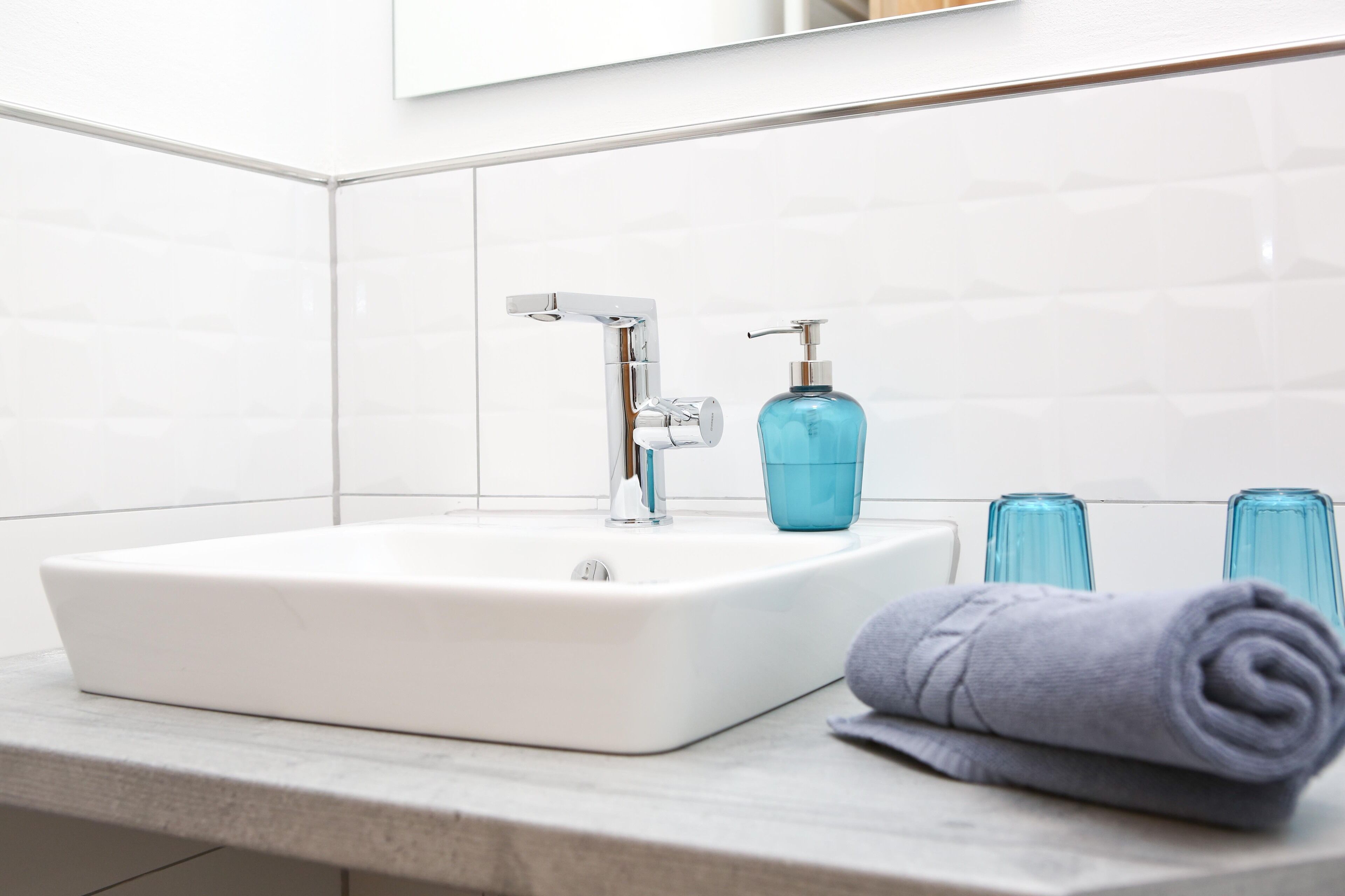 Een badkamer met een witte wasbak, een moderne kraan en een blauwe zeepdispenser.