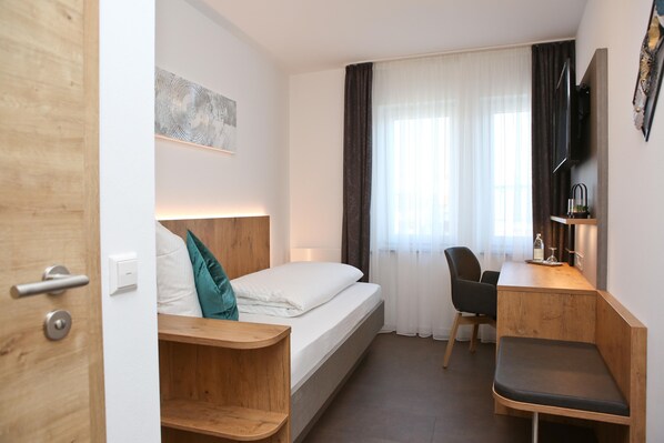 A hotel room with a bed, a desk, a chair, a wooden shelf, a TV, and a window with curtains. - Gasthof Adler (Hettingen)