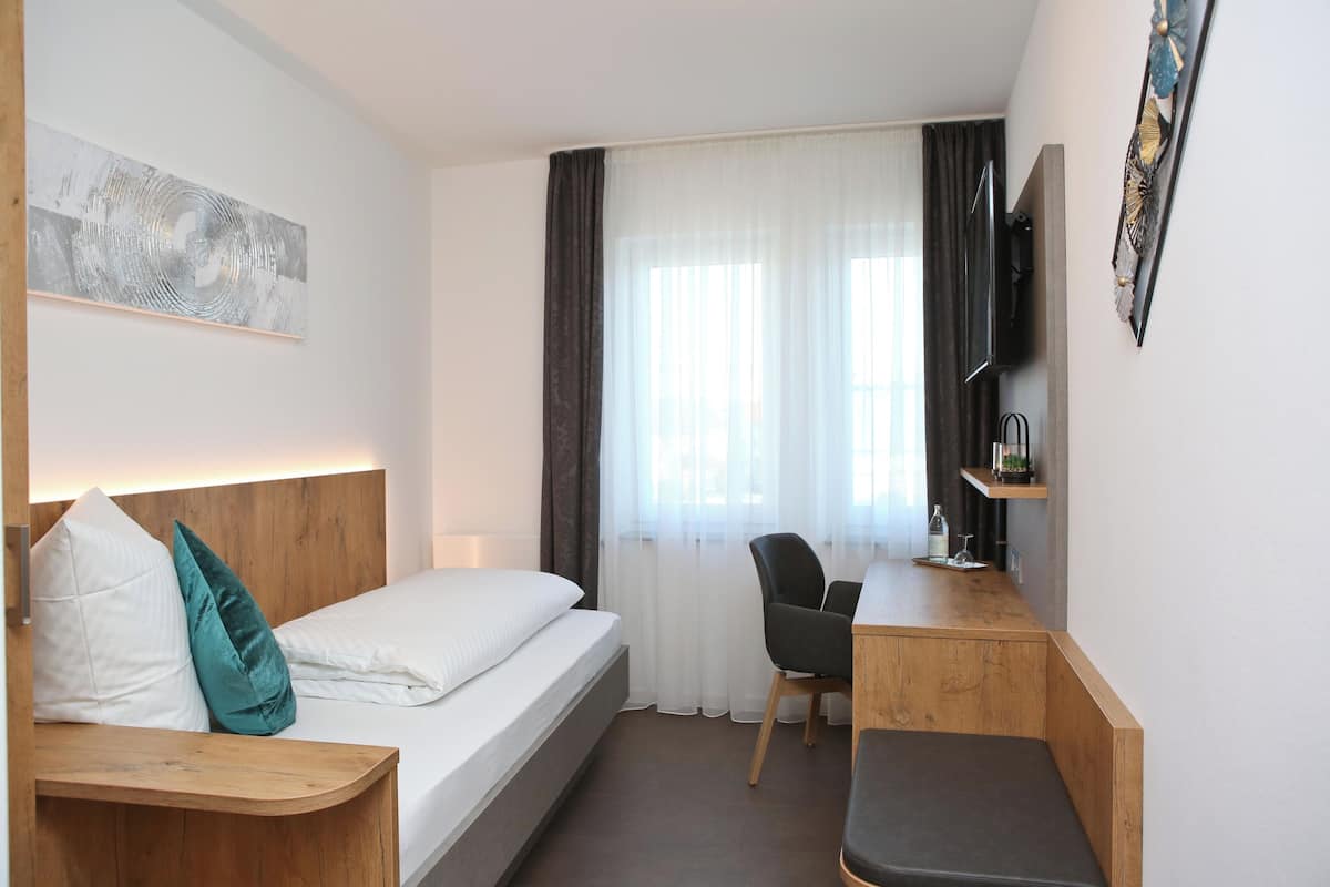 Quarto de hotel com cama, escrivaninha, cadeira, televisão e um quadro na parede.