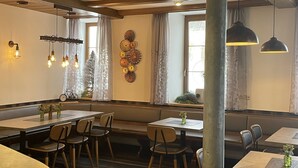 A restaurant interior with wooden beams, pendant lighting, and a decorative wall piece. Tables and chairs are arranged for dining. - Gasthof Adler (Hettingen)
