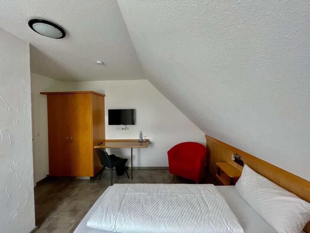 Et lille, moderne værelse med seng, skrivebord, rød stol og garderobeskab.