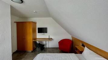 Et lille, moderne værelse med seng, skrivebord, rød stol og garderobeskab.