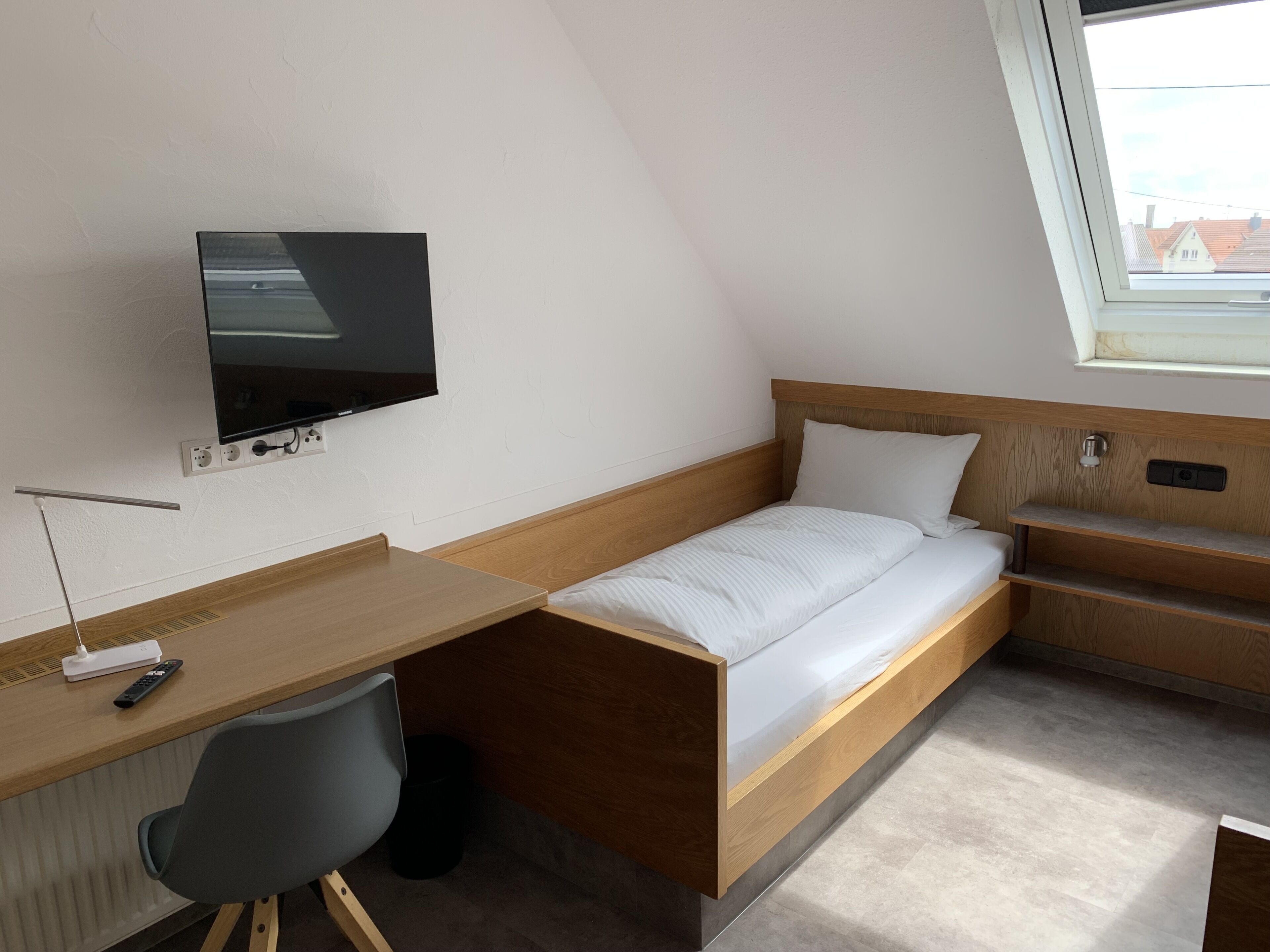 Una habitación pequeña con una cama, un escritorio y una televisión.
