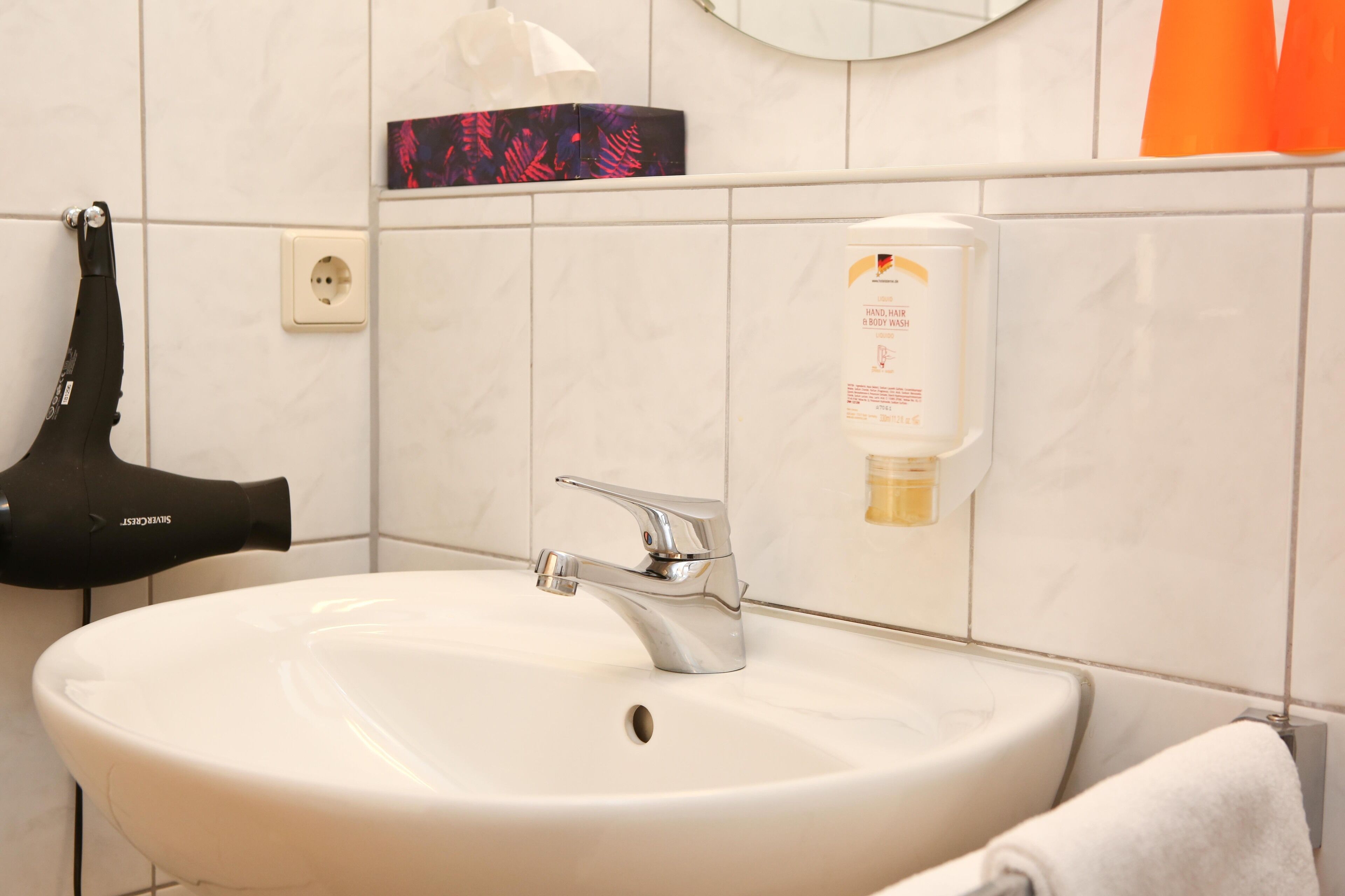 Un baño con lavamanos blanco, un secador de pelo y dispensador de jabón para manos.