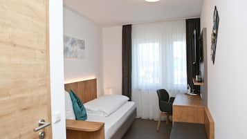 A hotel room with a bed, a desk, a chair, a TV, and a window with curtains.
