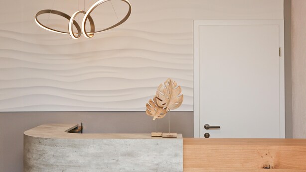 A reception desk with a concrete top and a wooden base, a wall-mounted leaf sculpture, and a hanging light fixture. - Gasthof Adler (Hettingen)