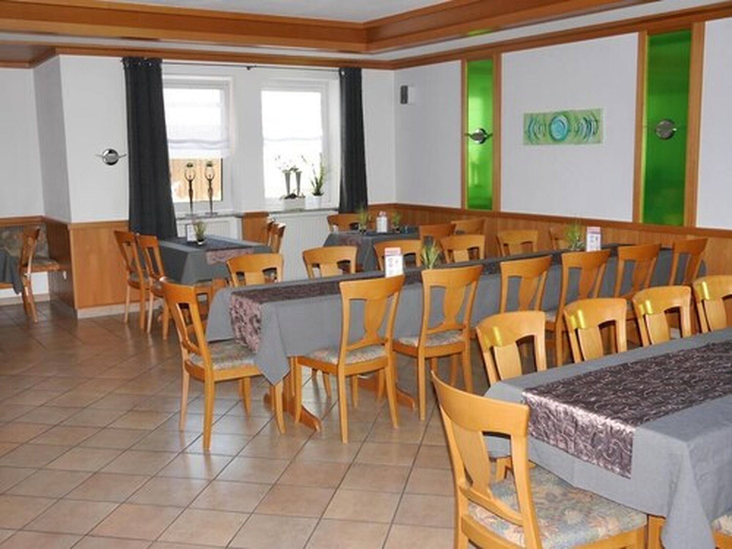 Un comedor con sillas y mesas de madera, una barra con el menú, y vistas al exterior a través de amplias ventanas.
