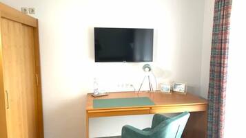 Quarto com escrivaninha de madeira, cadeira verde-água, televisão de tela plana na parede e guarda-roupa de madeira.