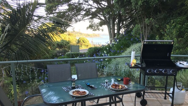 An outdoor dining area with a table set for two, a grill, and a view of a body of water. - Bay of Islands Gateway Motel (Paihia)