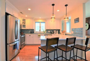 A modern kitchen with white cabinets, stainless steel appliances, a central island with bar stools, and pendant lighting. - Less Than 2 Blocks to Sand & Sea at 6 Philadelphia Square, Rehoboth Beach! (Rehoboth Beach)