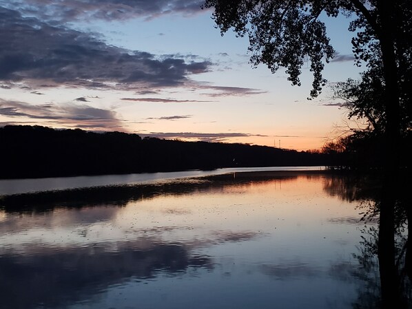 Un río tranquilo al atardecer, con la silueta de árboles a la derecha y un cielo nublado.