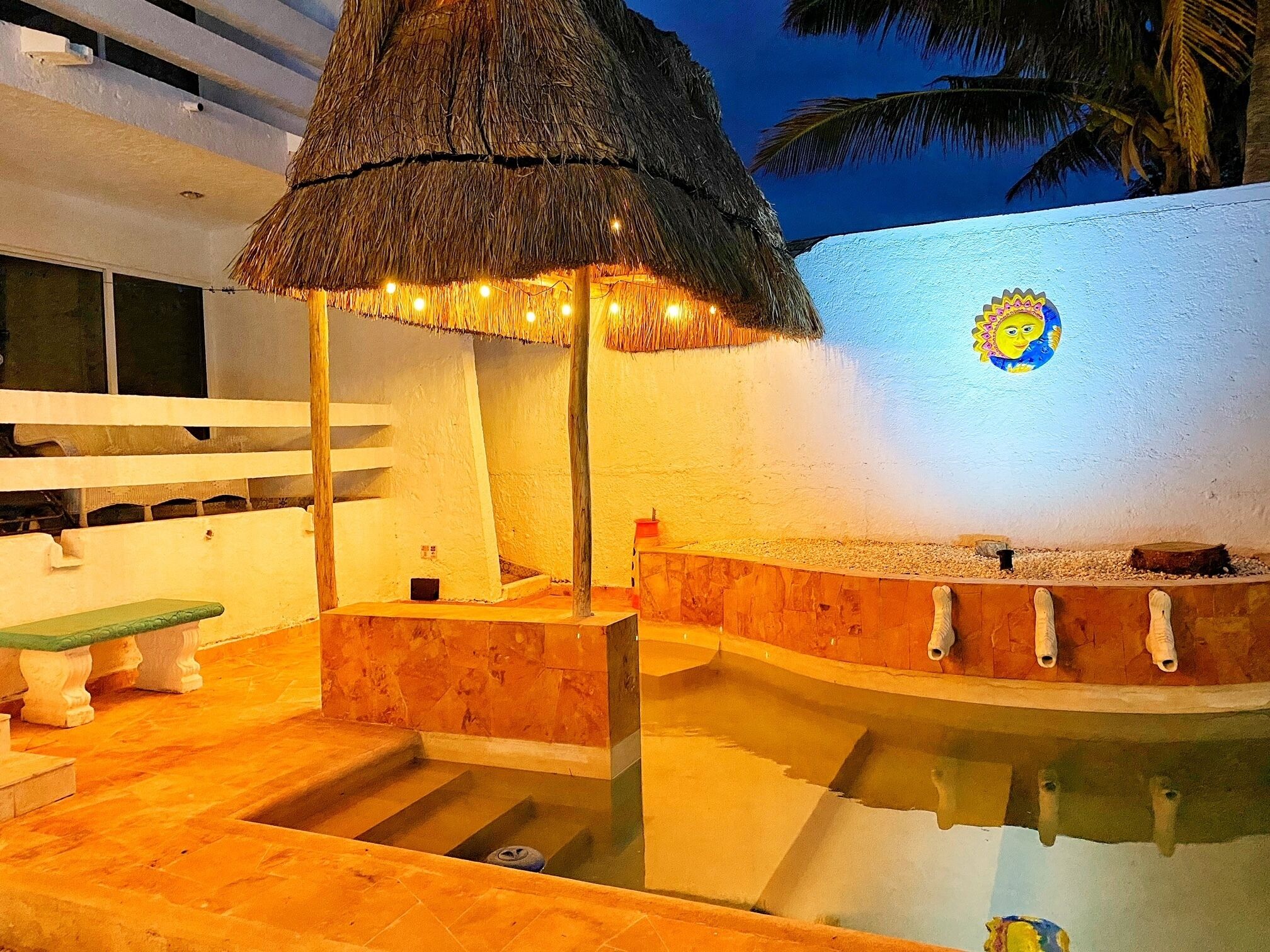 A pool area with a thatched roof, a bench, and a decorative wall.