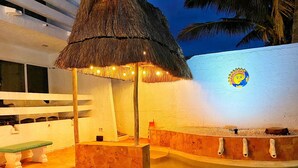 Un espace piscine agrémenté d’un toit de chaume, d’un banc et d’un mur décoratif.